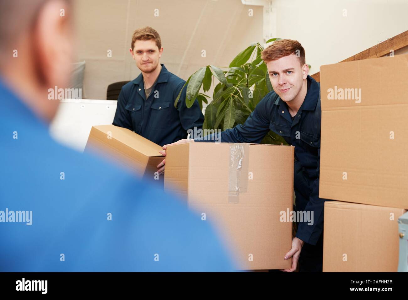 Removal Company Workers Unloading Furniture And Boxes From Truck Into New Home On Moving Day Stock Photo