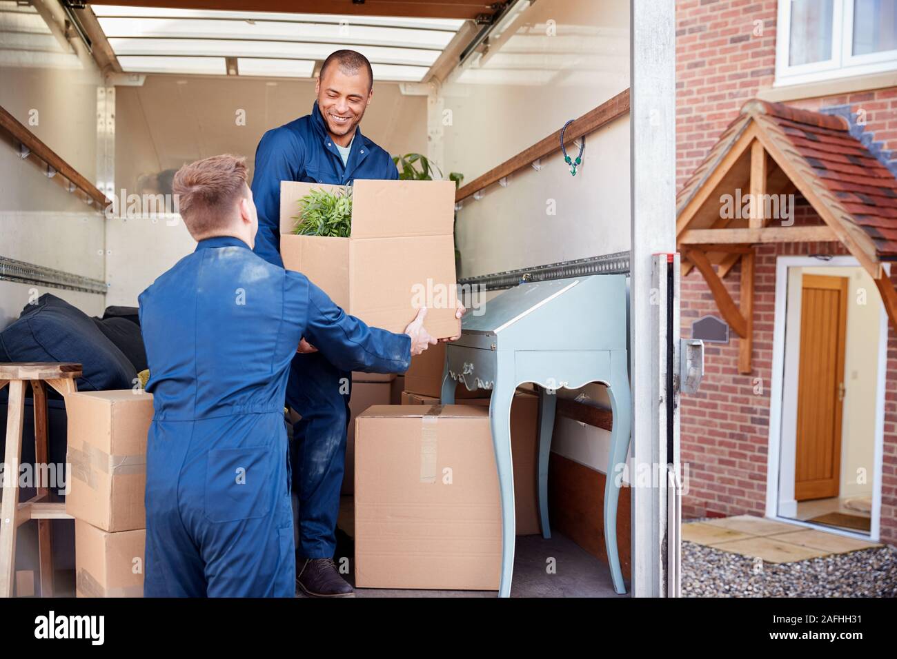 Removal Company Workers Unloading Furniture And Boxes From Truck Into New Home On Moving Day Stock Photo