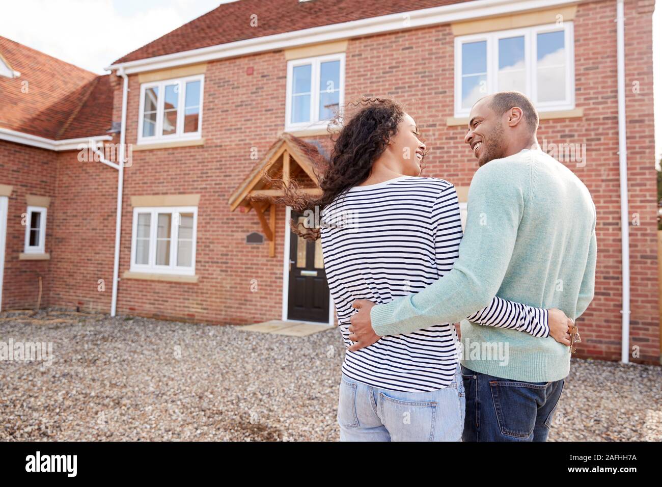 Rear View Of Couple Standing Outside New Home On Moving Day Looking At House Stock Photo