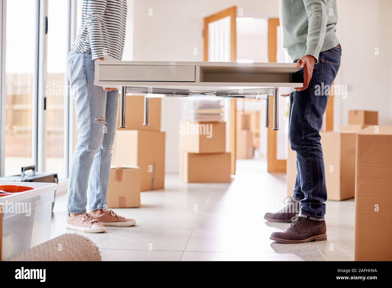 Close Up Of Couple In New Home On Moving Day Carrying Table Together Stock Photo
