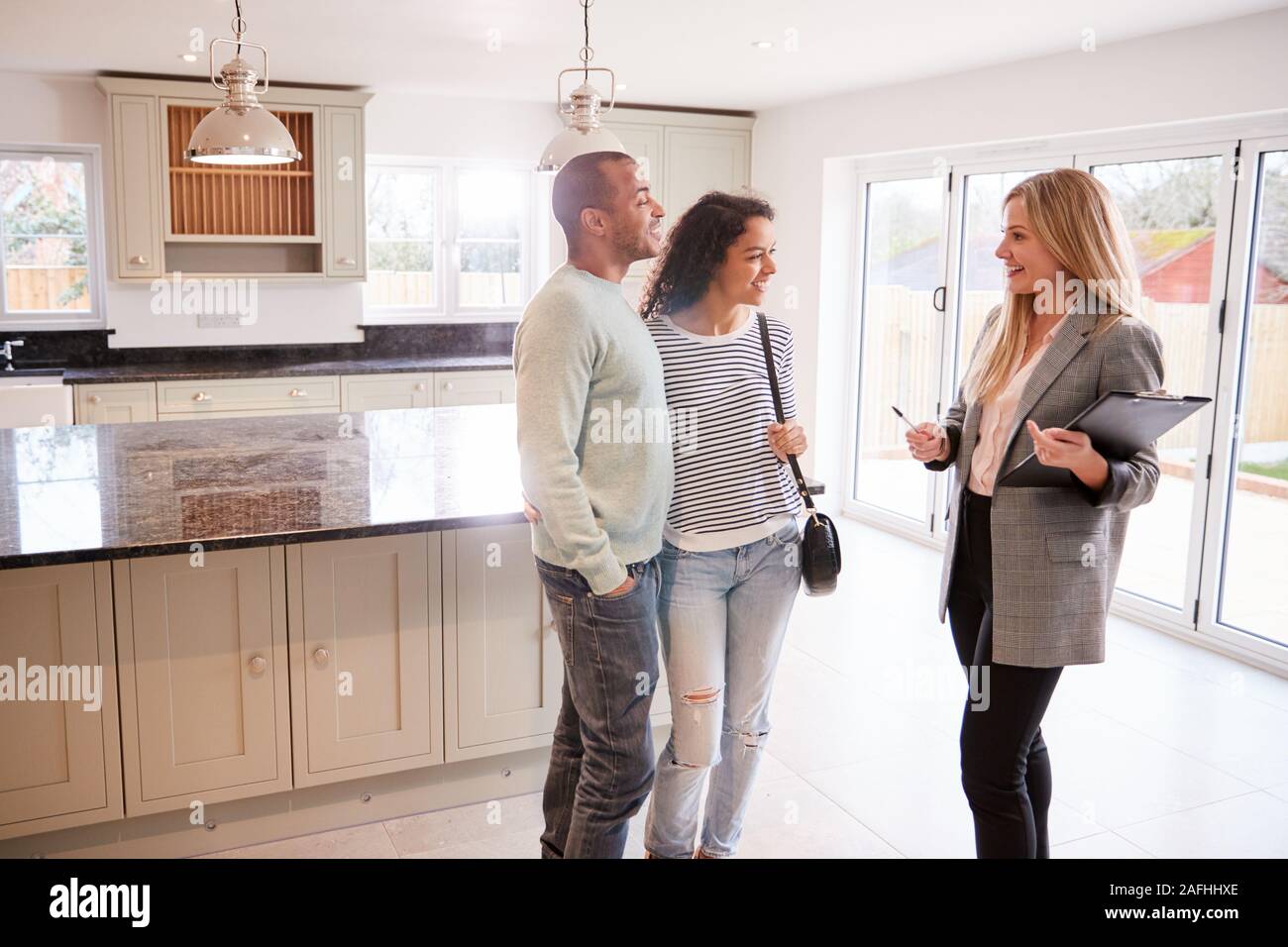 Female Realtor Showing Couple Interested In Buying Around House Stock Photo