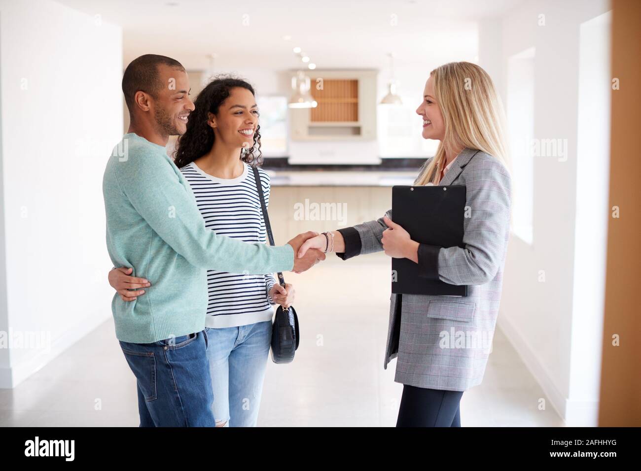 Female Realtor Shaking Hands With Couple Interested In Buying House Stock Photo