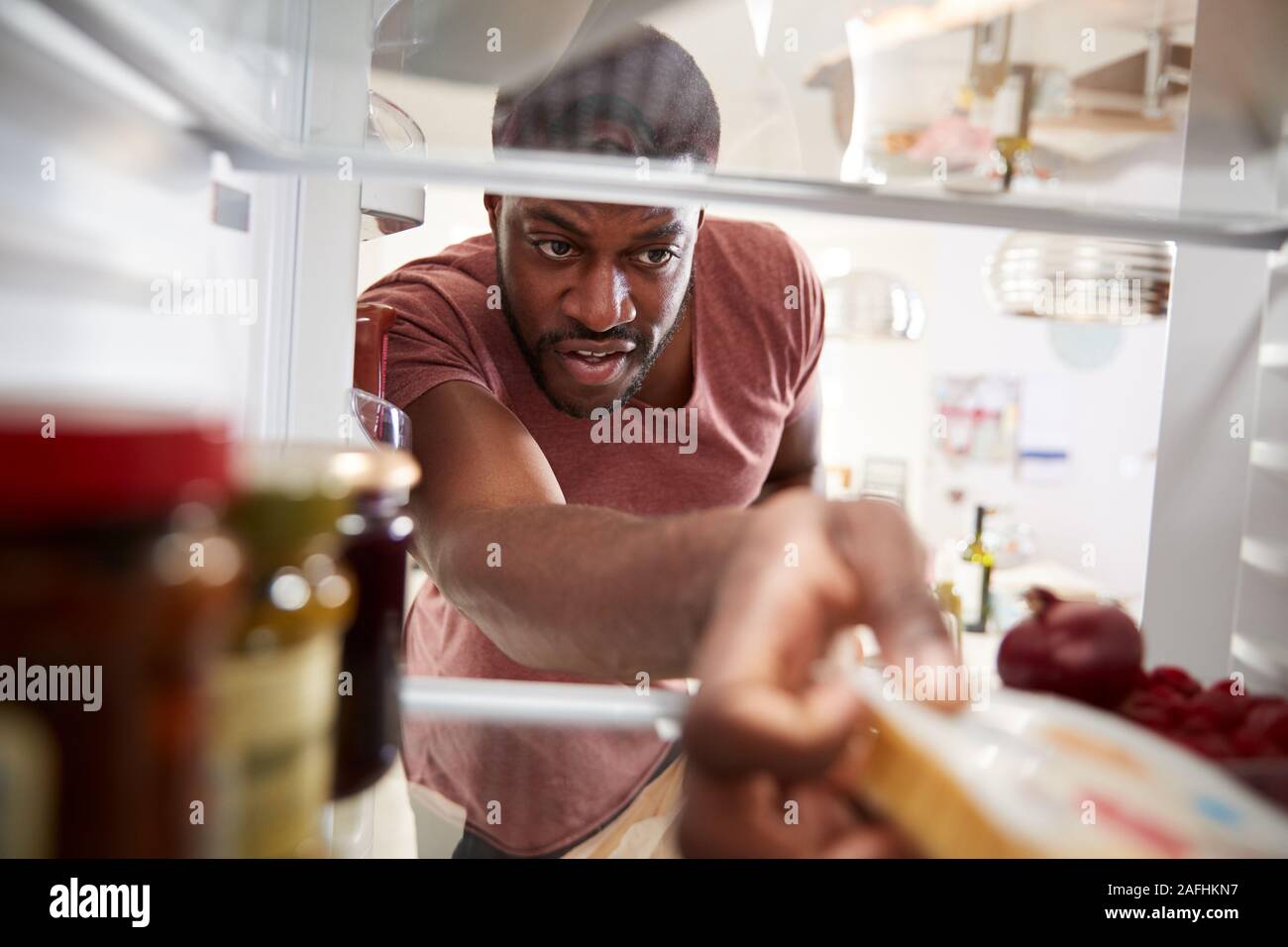 View Looking Out From Inside Of Refrigerator As Man Opens Door And Unpacks Shopping Bag Of Food Stock Photo