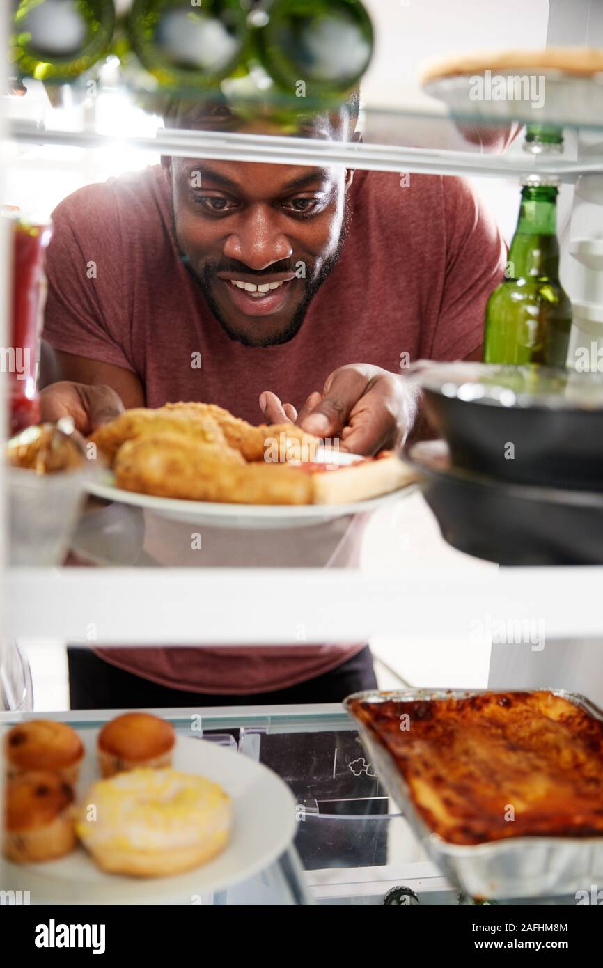 View Looking Out From Inside Of Refrigerator Filled With Unhealthy Takeaway Food As Man Opens Door Stock Photo