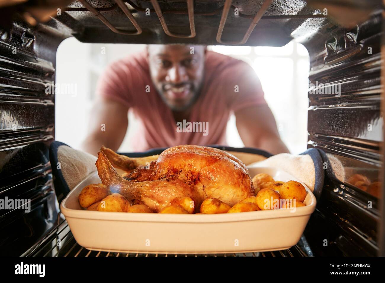 View Looking Out From Inside Oven As Man Cooks Sunday Roast Chicken Dinner Stock Photo
