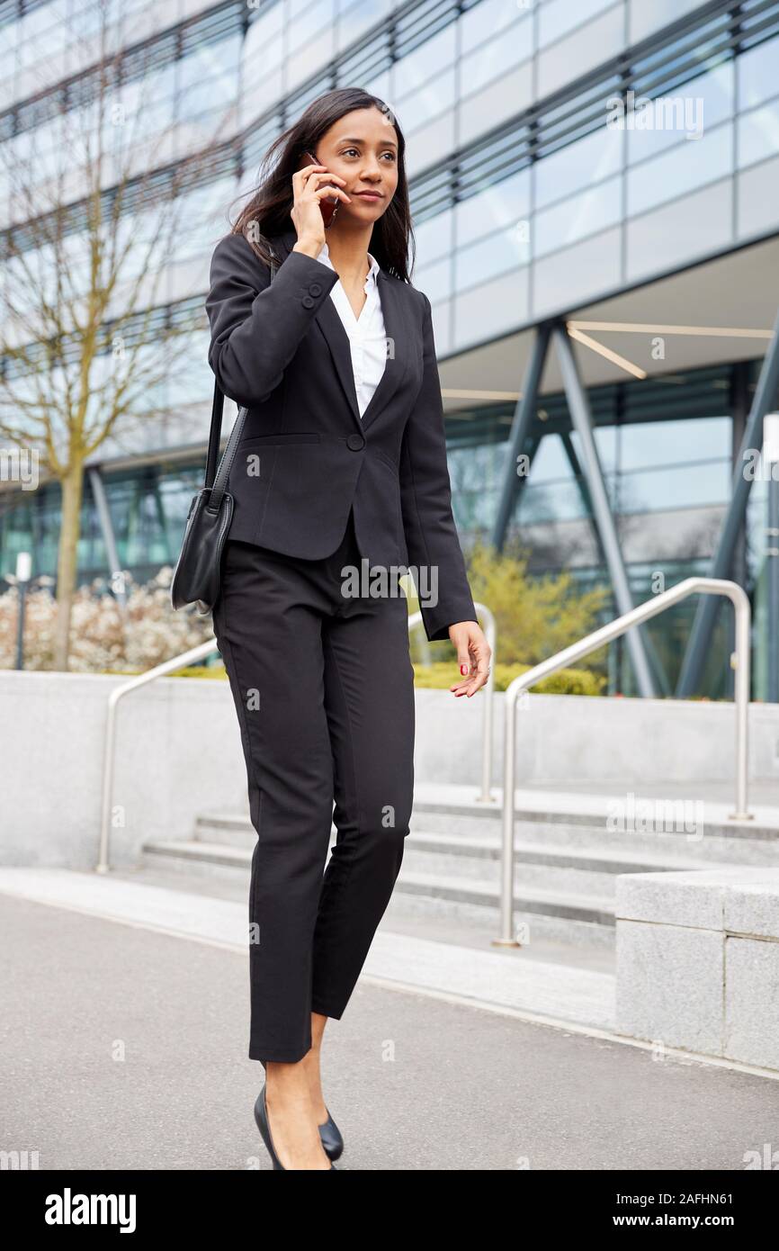 Businesswoman Commuting To Work Talking On Mobile Phone Outside Modern Office Building Stock Photo