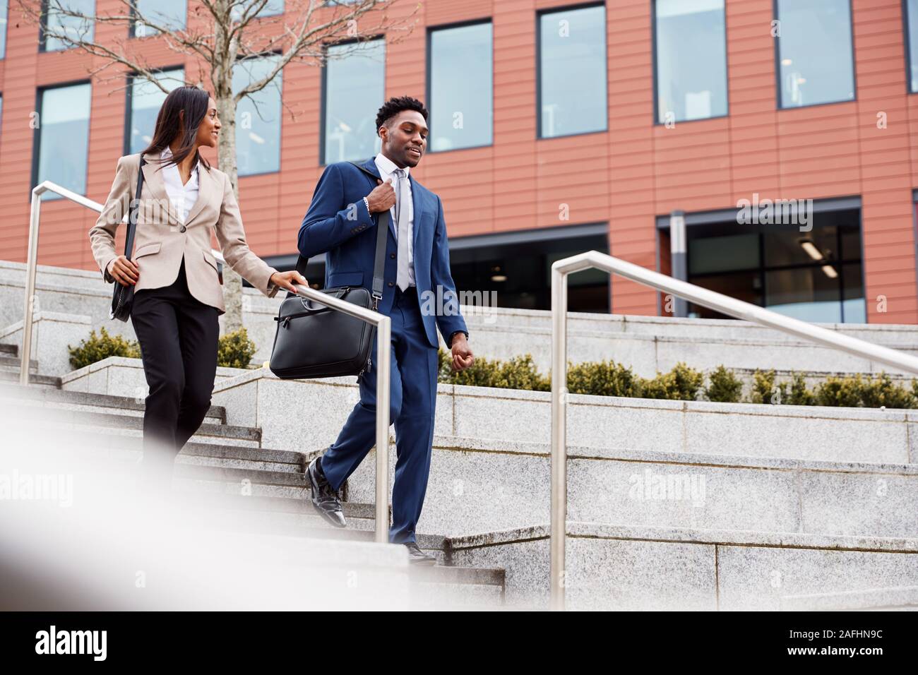 Businessman And Businesswoman Commuting To Work Walking Down Steps Outside Office Building Stock Photo