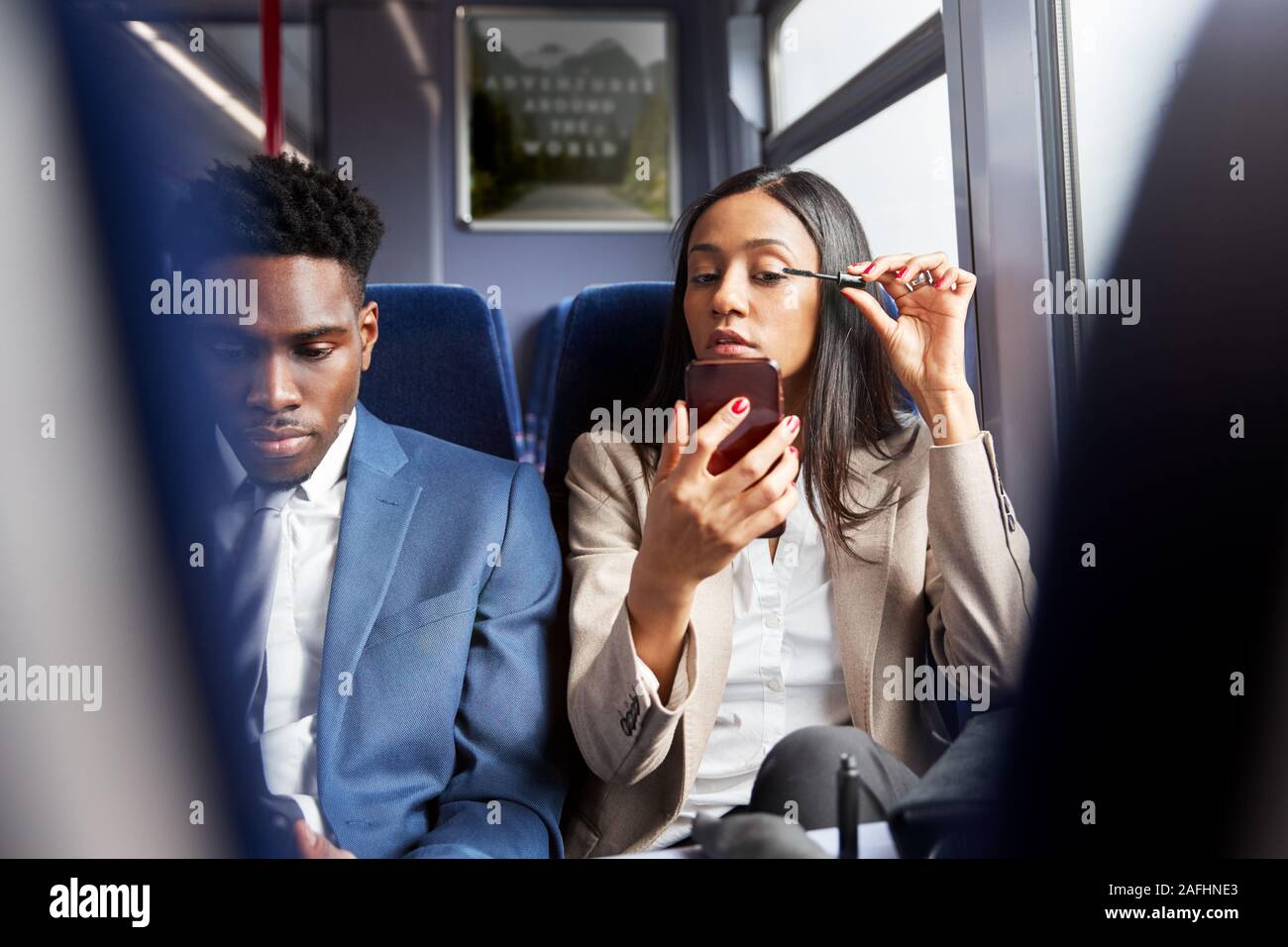 Businesswoman Sitting In Train Commuting To Work Putting On Make Up Stock Photo