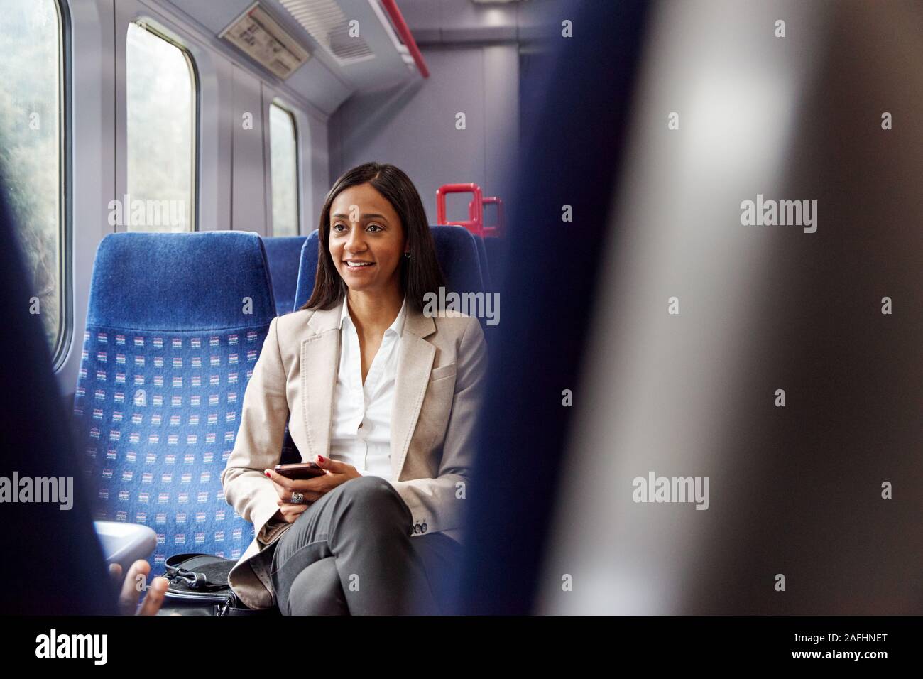 Businesswoman Sitting In Train Commuting To Work Checking Messages On Mobile Phone Stock Photo