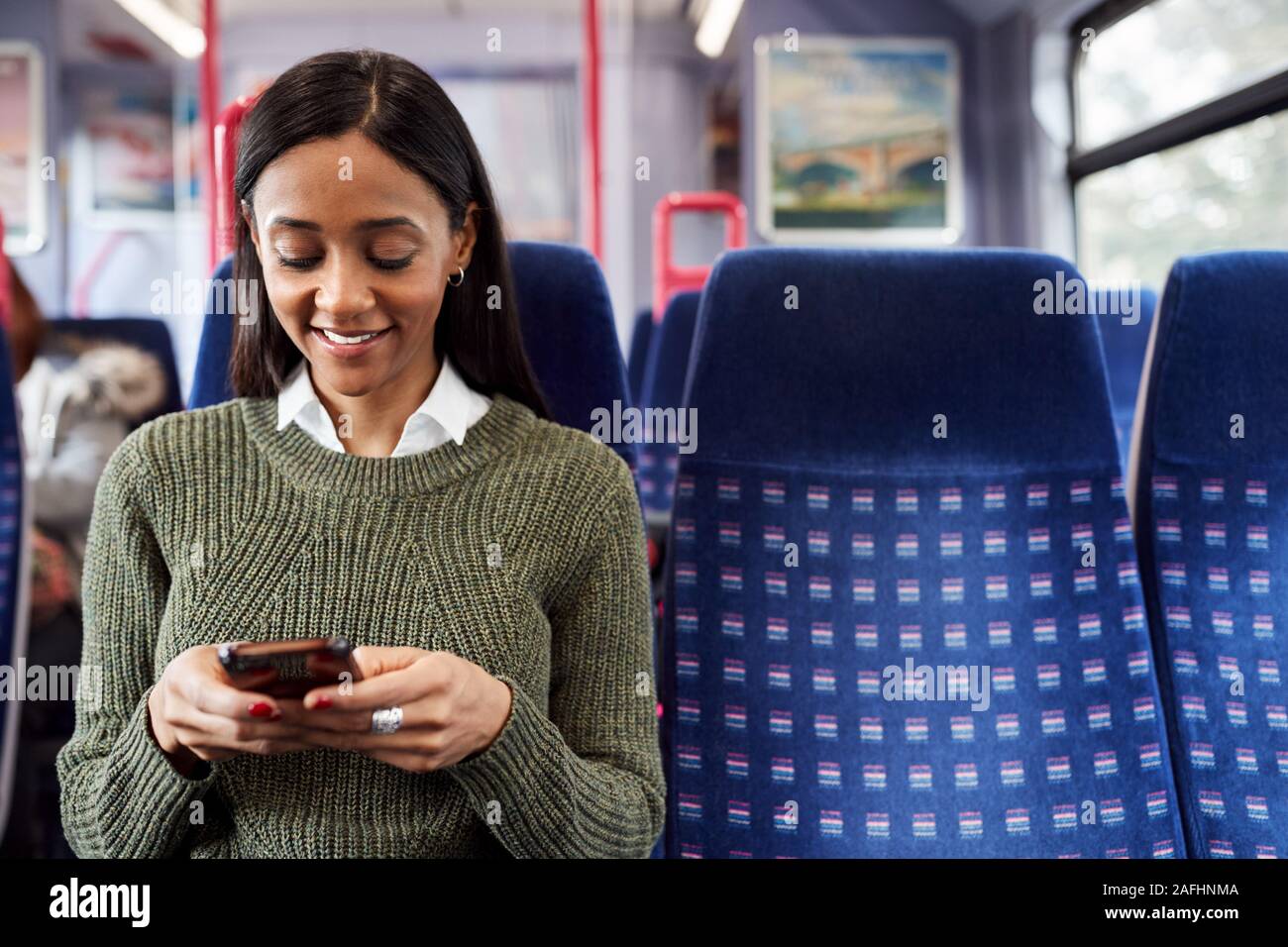 Female Passenger Sitting In Train Looking At Mobile Phone Stock Photo