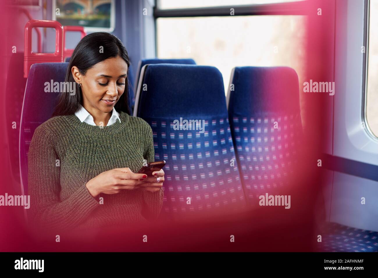 Female Passenger Sitting In Train Looking At Mobile Phone Stock Photo