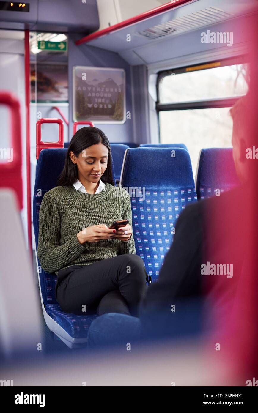 Female Passenger Sitting In Train Looking At Mobile Phone Stock Photo