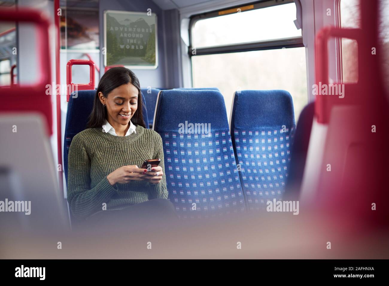 Female Passenger Sitting In Train Looking At Mobile Phone Stock Photo