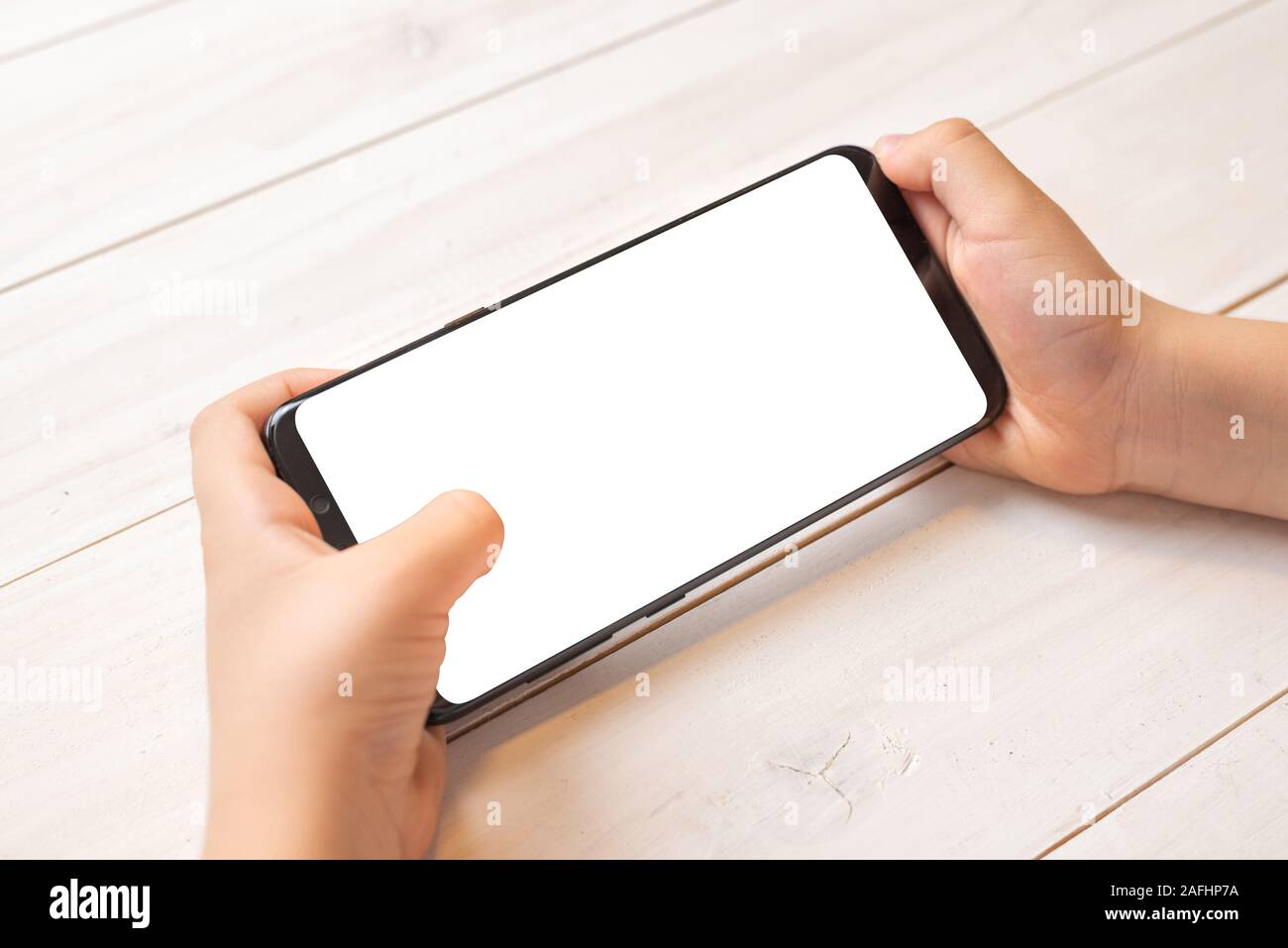 Smart phone mockup in kid hands in horizontal position. Isolated screen in white for promote game or mobile app Stock Photo
