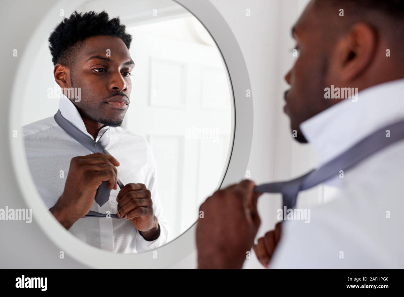 Businessman At Home Tying Necktie In Mirror Before Leaving For Work Stock Photo