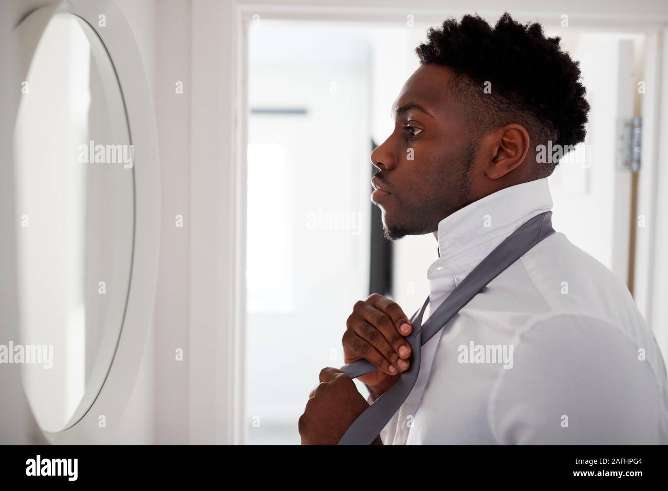 Businessman At Home Tying Necktie In Mirror Before Leaving For Work Stock Photo