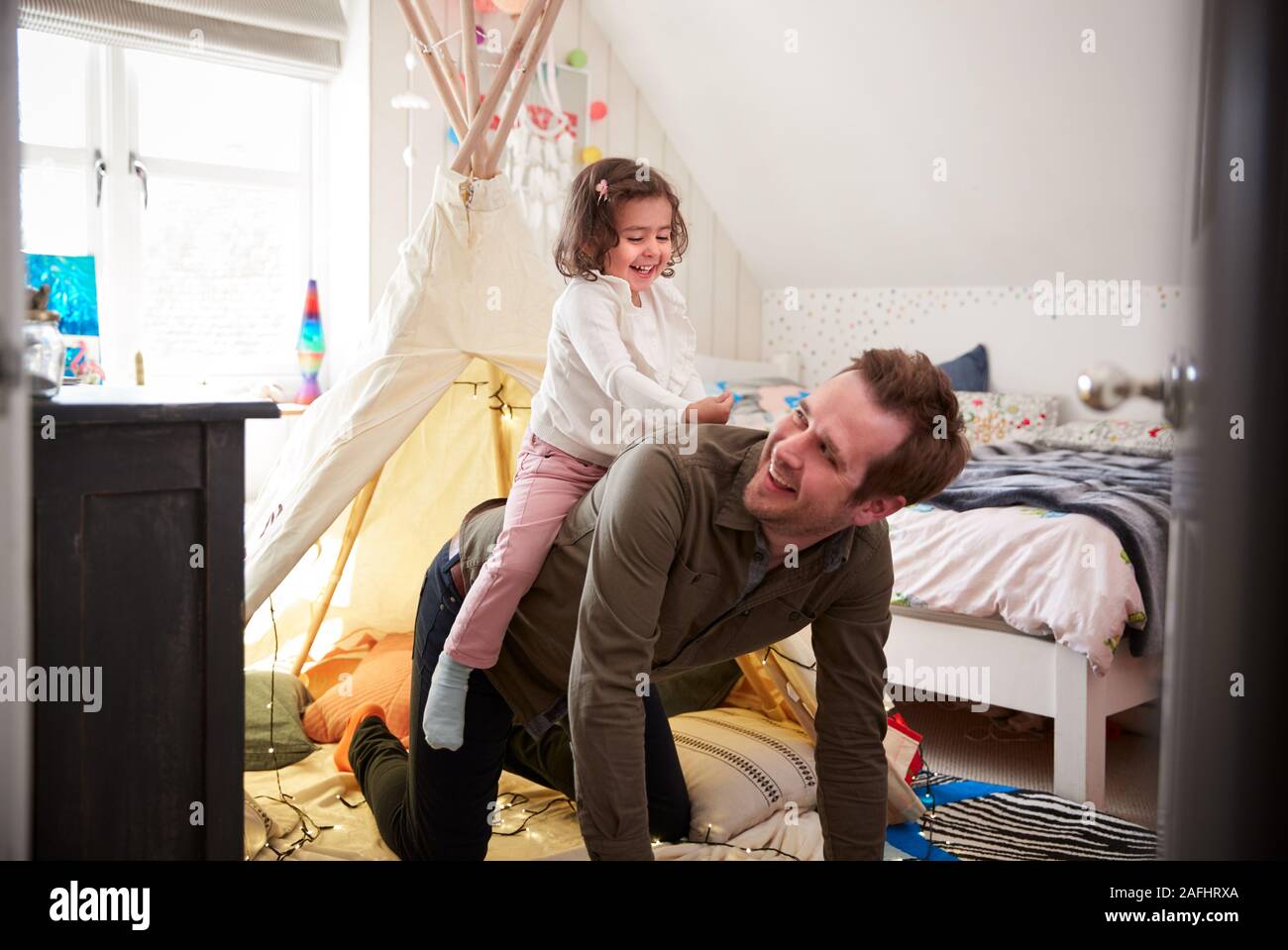 Daughter Riding On Fathers Back As They Play In Den In Bedroom At Home Stock Photo