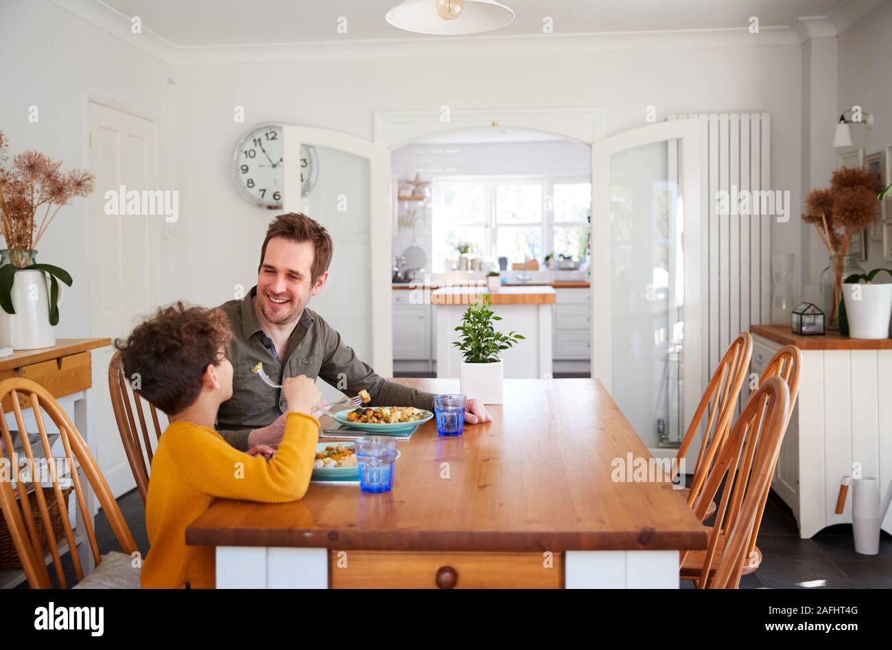 Single Father Sitting At Table Eating Meal With Son In Kitchen At Home Stock Photo