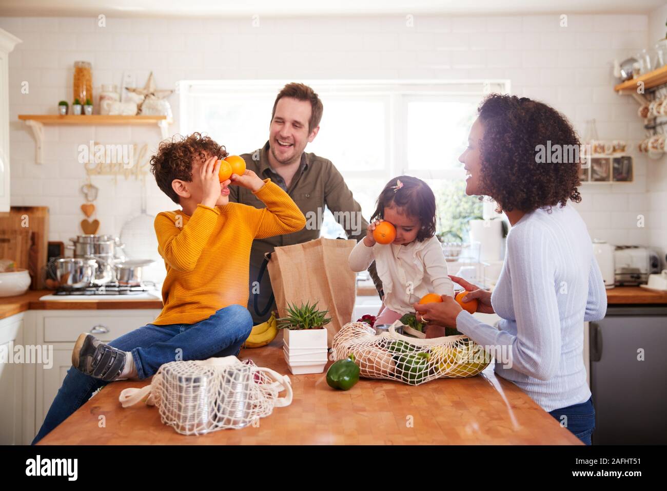 Family Returning Home From Shopping Trip Using Plastic Free Bags Unpacking Groceries In Kitchen Stock Photo