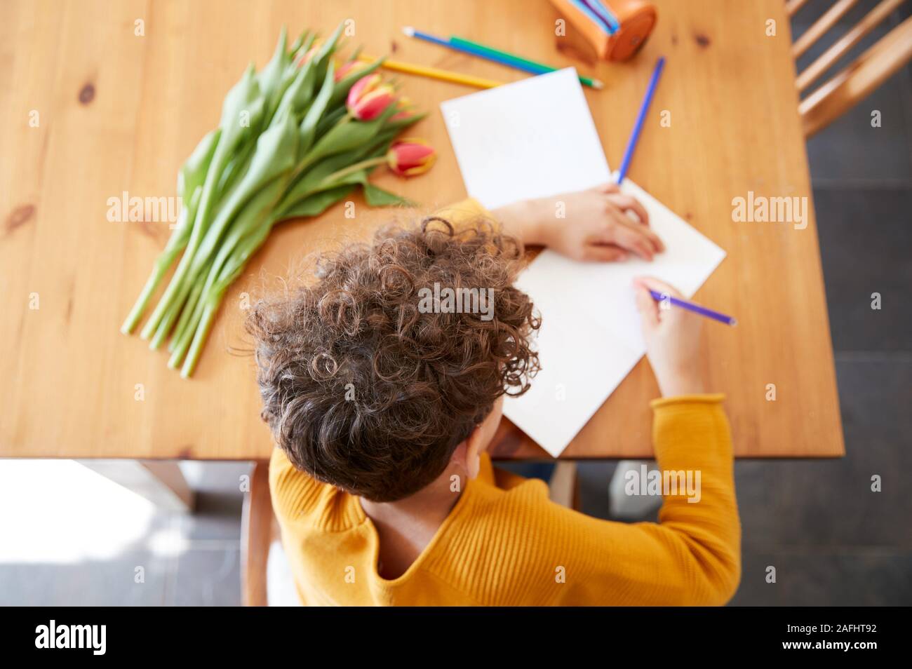 Overhead Shot Of Young Boy At Home With Bunch Of Flowers Writing In Mothers Day Card Stock Photo