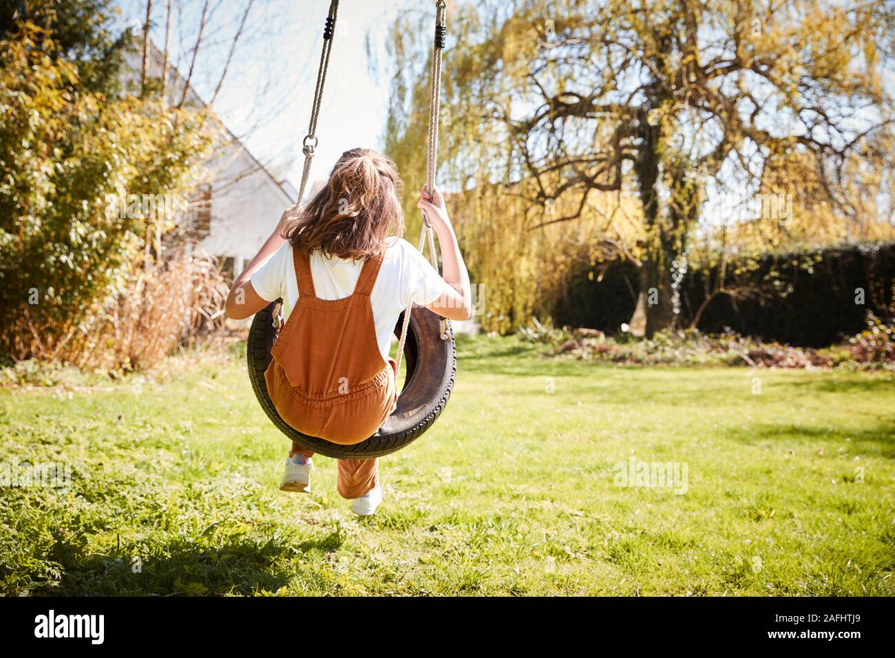 Rear View Of Girl Having Fun On Tyre Swing In Garden At Home Stock Photo