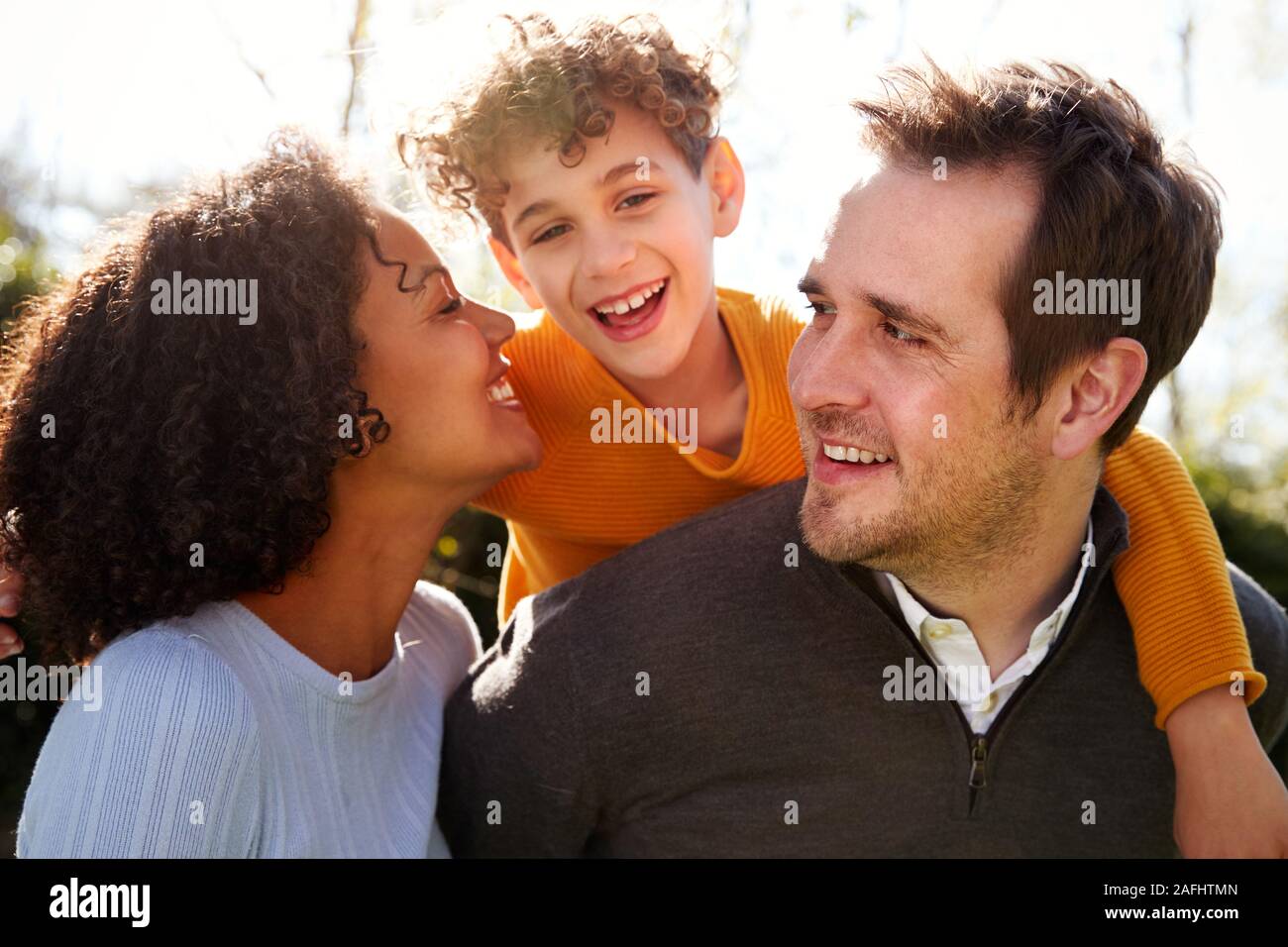 Outdoor Portrait Of Smiling Family In Garden At Home Against Flaring Sun Stock Photo
