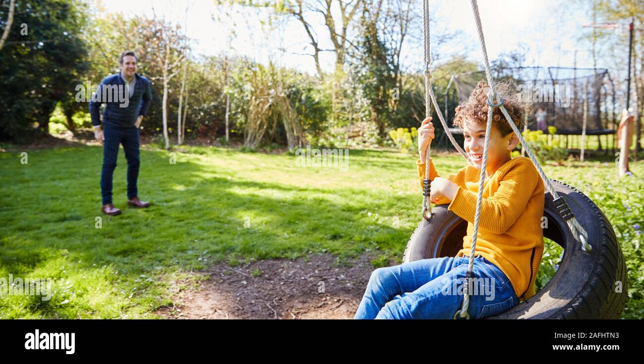 Father And Son Having Fun On Tyre Swing In Garden At Home Stock Photo
