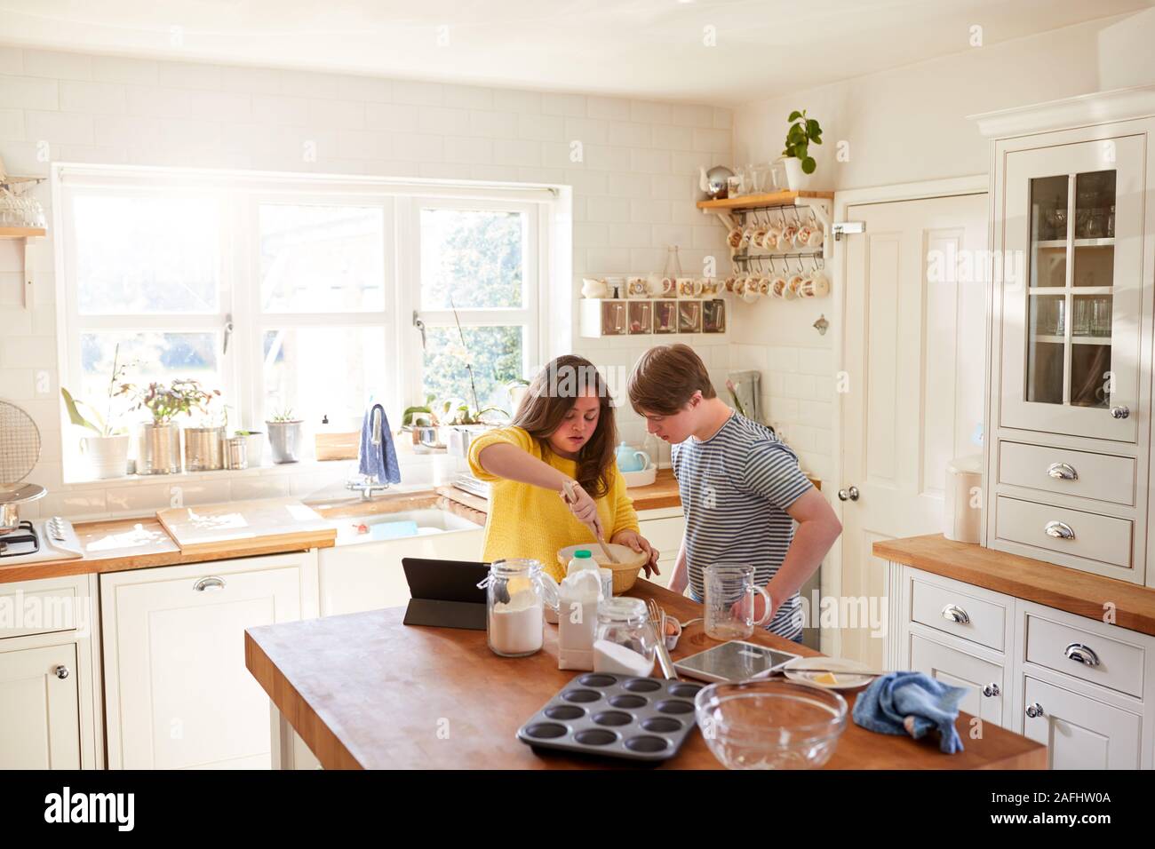 Young Downs Syndrome Couple Following Recipe On Digital Tablet To Bake Cake In Kitchen At Home Stock Photo