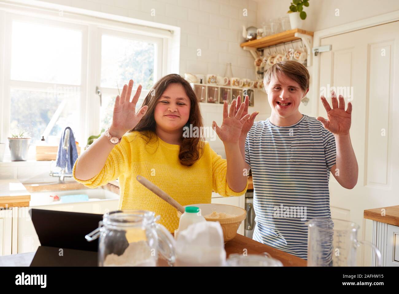 Portrait Of Downs Syndrome Couple Following Recipe On Digital Tablet To Bake Cake In Kitchen At Home Stock Photo