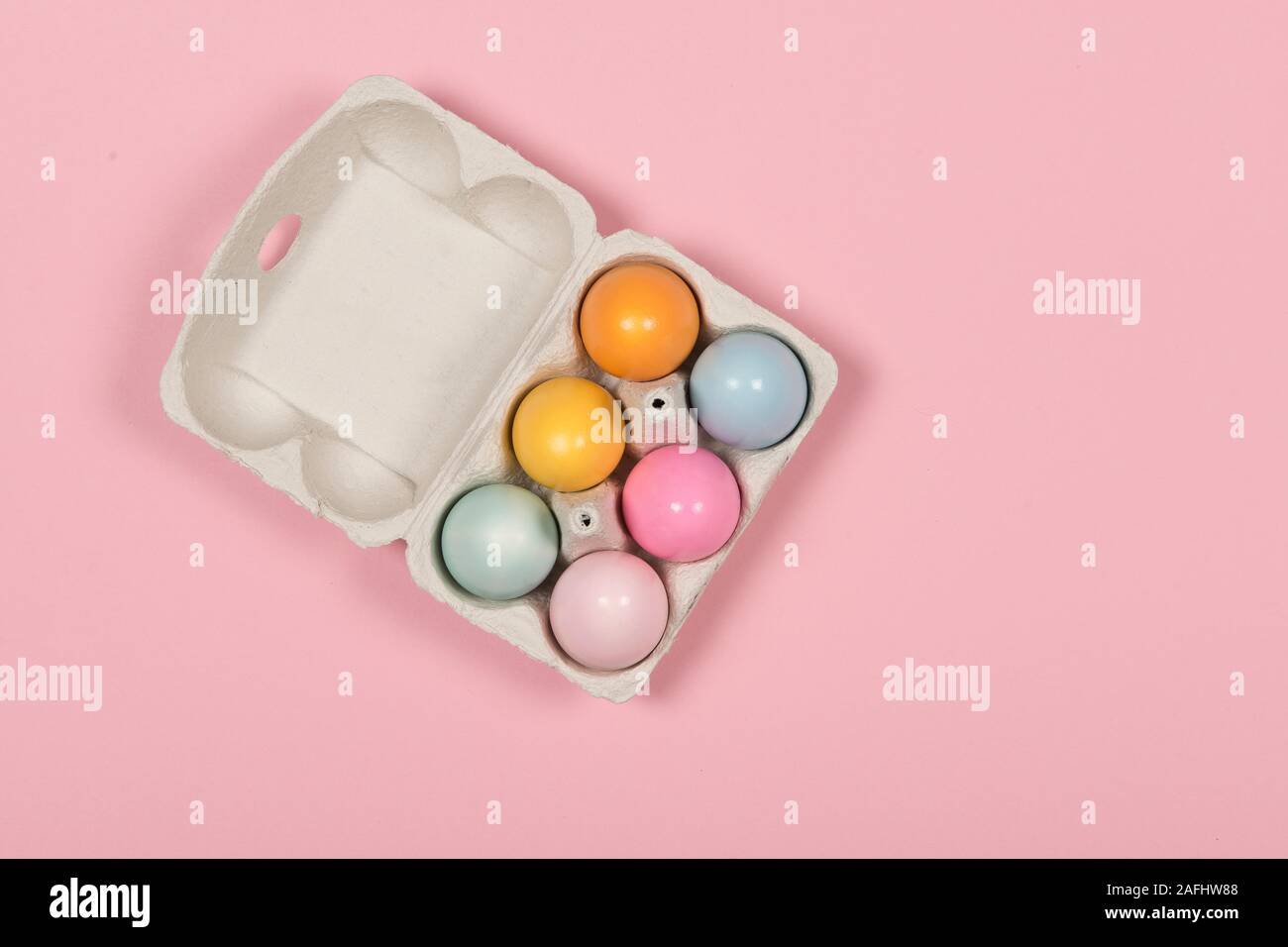 Easter background with a carton egg box with pastel colored easter eggs in it on a pink background Stock Photo