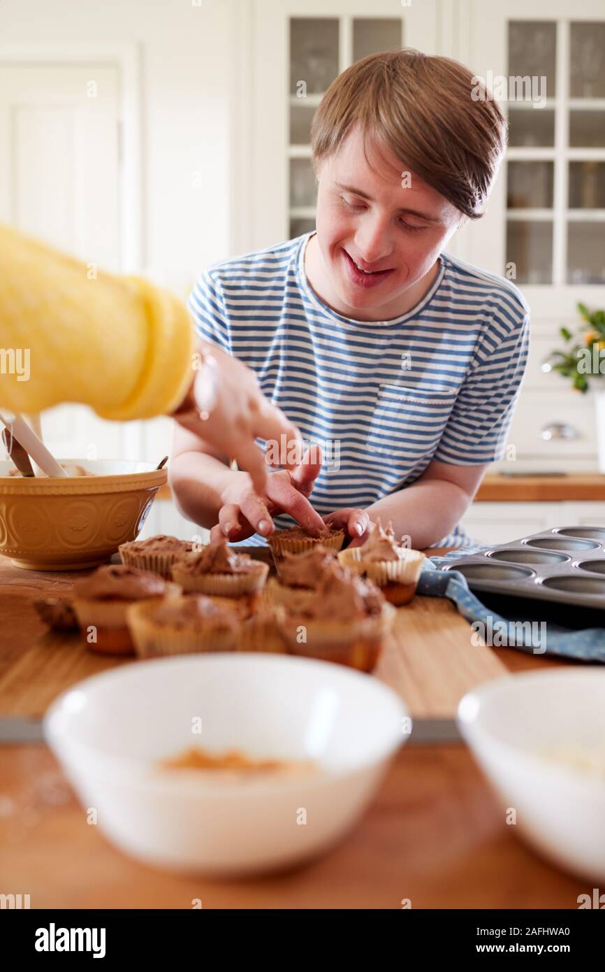 Young Downs Syndrome Couple Decorating Homemade Cupcakes With Icing In Kitchen At Home Stock Photo