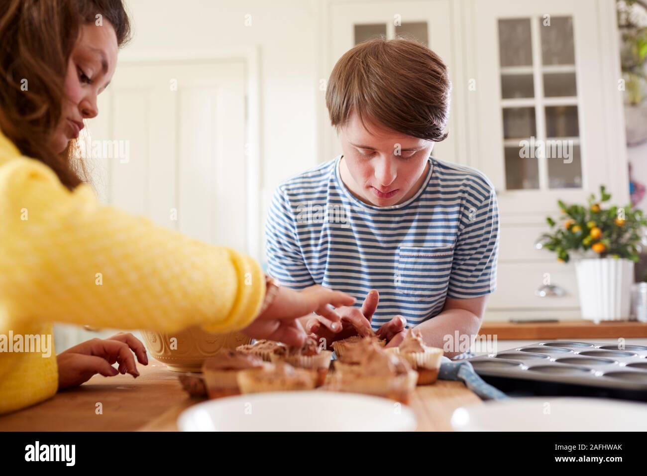 Young Downs Syndrome Couple Decorating Homemade Cupcakes With Icing In Kitchen At Home Stock Photo
