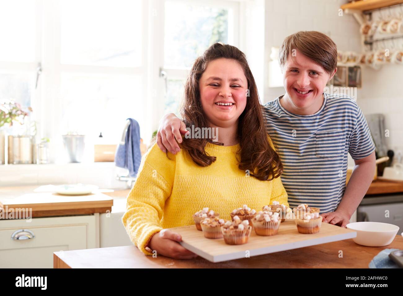 Portrait Of Downs Syndrome Couple Decorating Homemade Cupcakes With Marshmallows In Kitchen At Home Stock Photo