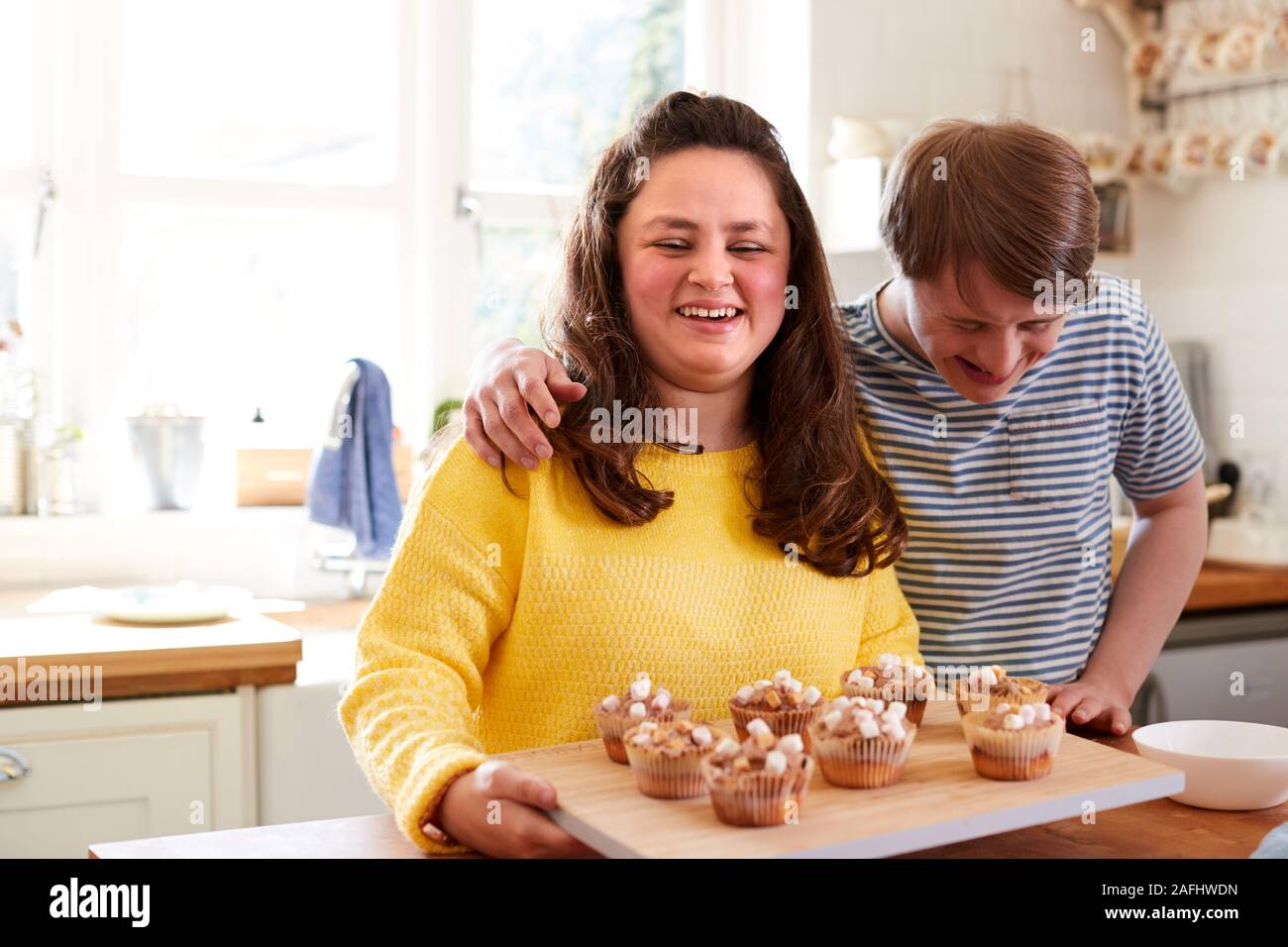 Portrait Of Downs Syndrome Couple Decorating Homemade Cupcakes With Marshmallows In Kitchen At Home Stock Photo