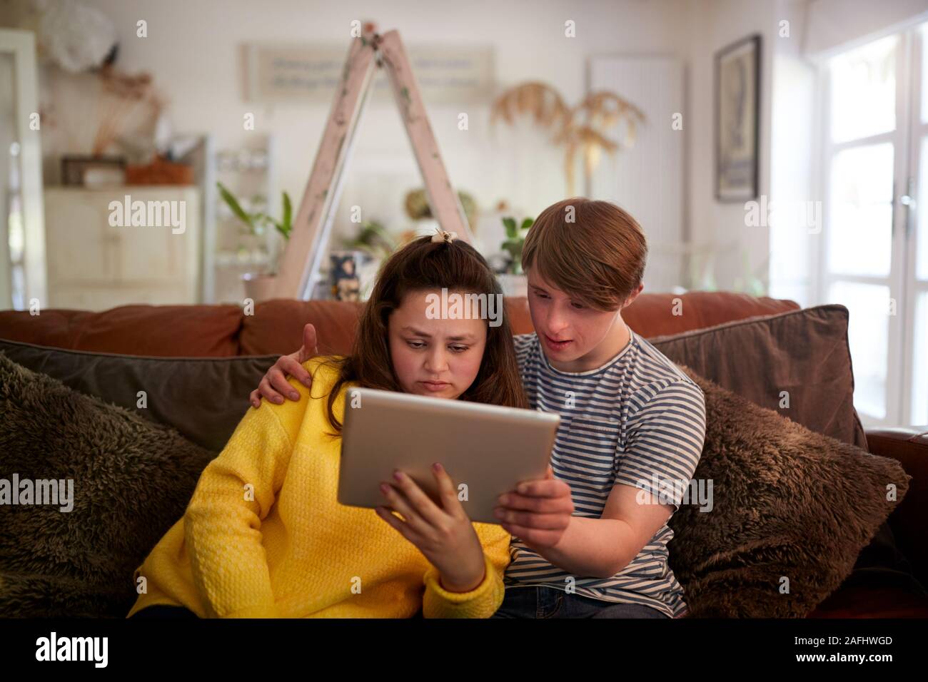 Young Downs Syndrome Couple Sitting On Sofa Using Digital Tablet At Home Stock Photo