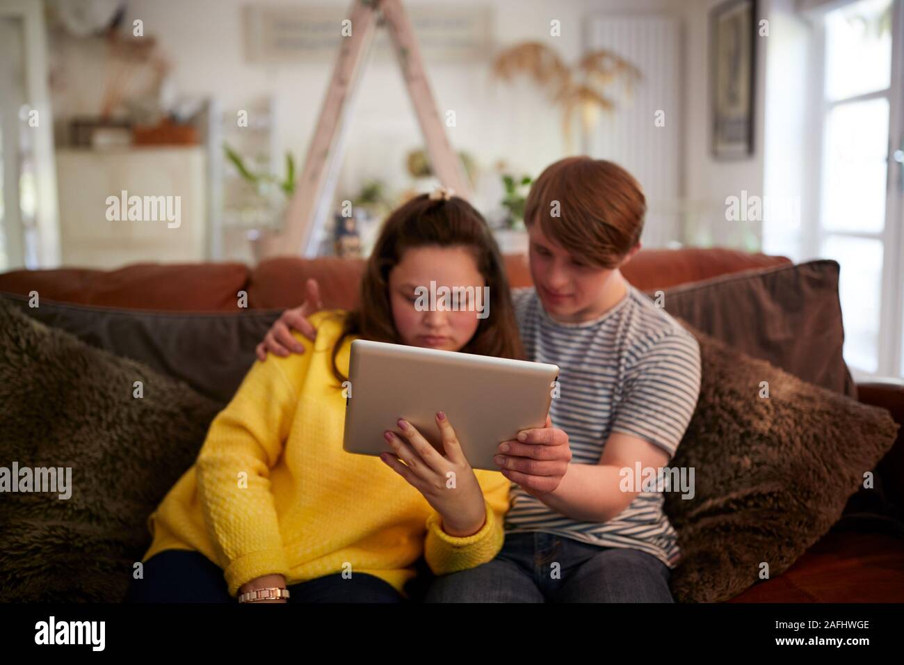 Young Downs Syndrome Couple Sitting On Sofa Using Digital Tablet At Home Stock Photo