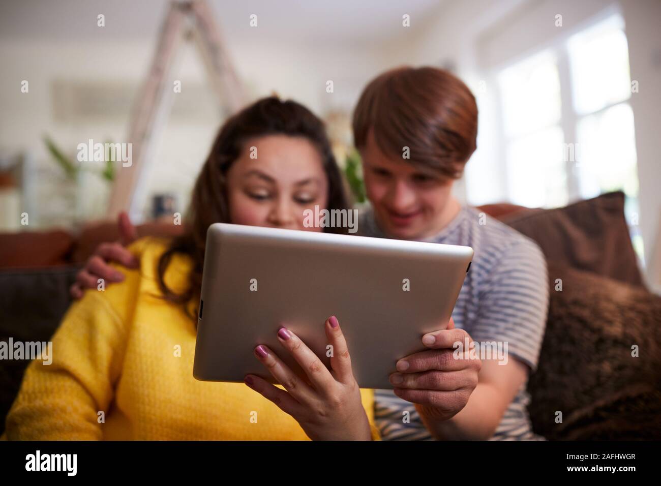 Young Downs Syndrome Couple Sitting On Sofa Using Digital Tablet At Home Stock Photo