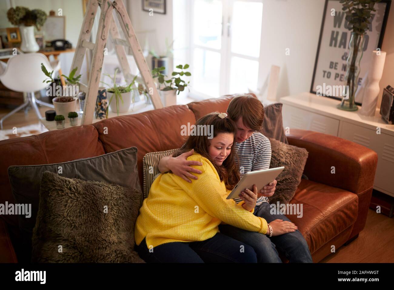 Young Downs Syndrome Couple Sitting On Sofa Using Digital Tablet At Home Stock Photo