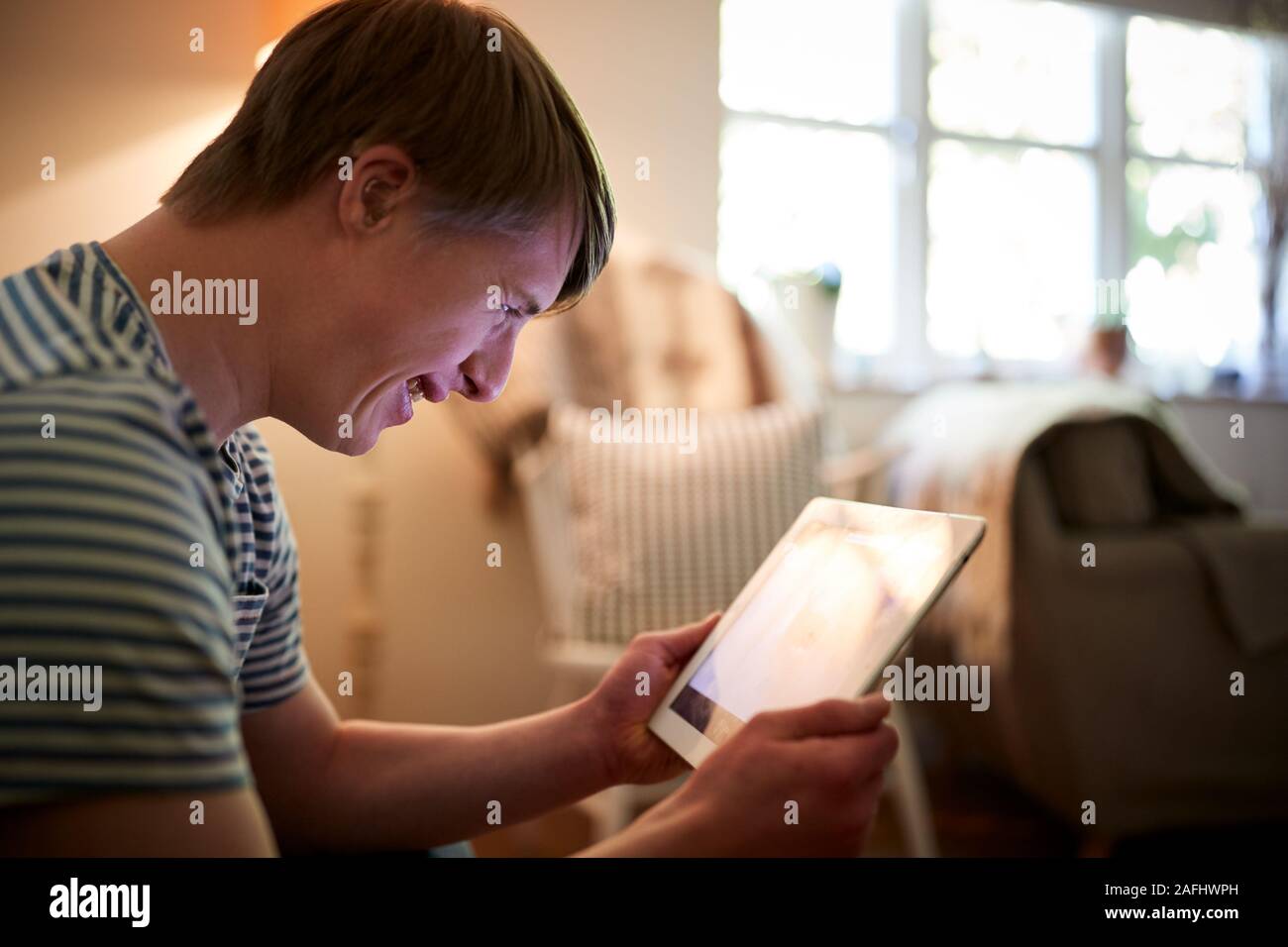 Young Downs Syndrome Man Sitting On Sofa Using Digital Tablet At Home Stock Photo