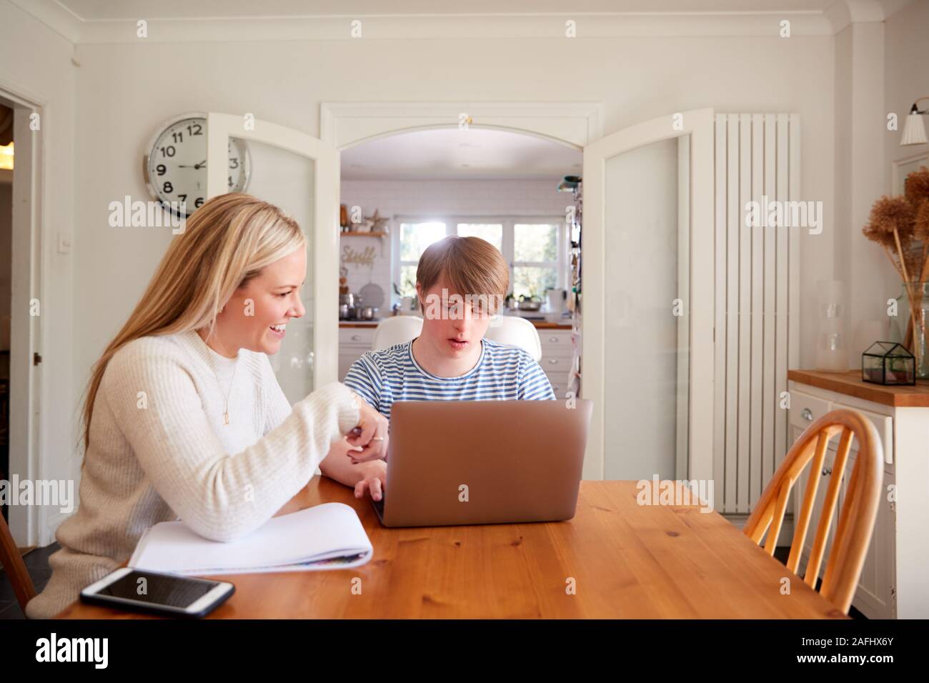 Downs Syndrome Man Sitting With Home Tutor Using Laptop For Lesson At Home Stock Photo