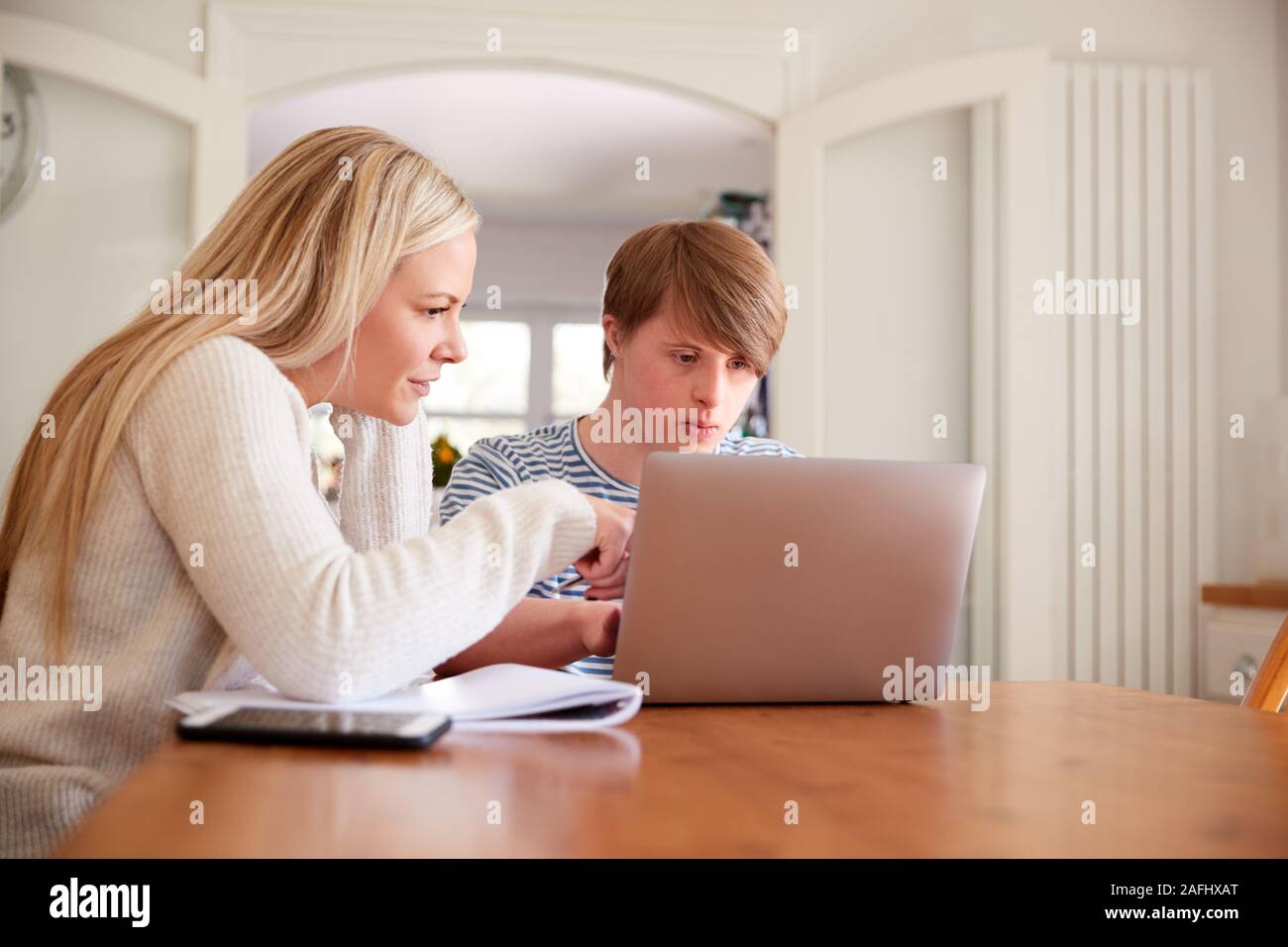 Downs Syndrome Man Sitting With Home Tutor Using Laptop For Lesson At Home Stock Photo