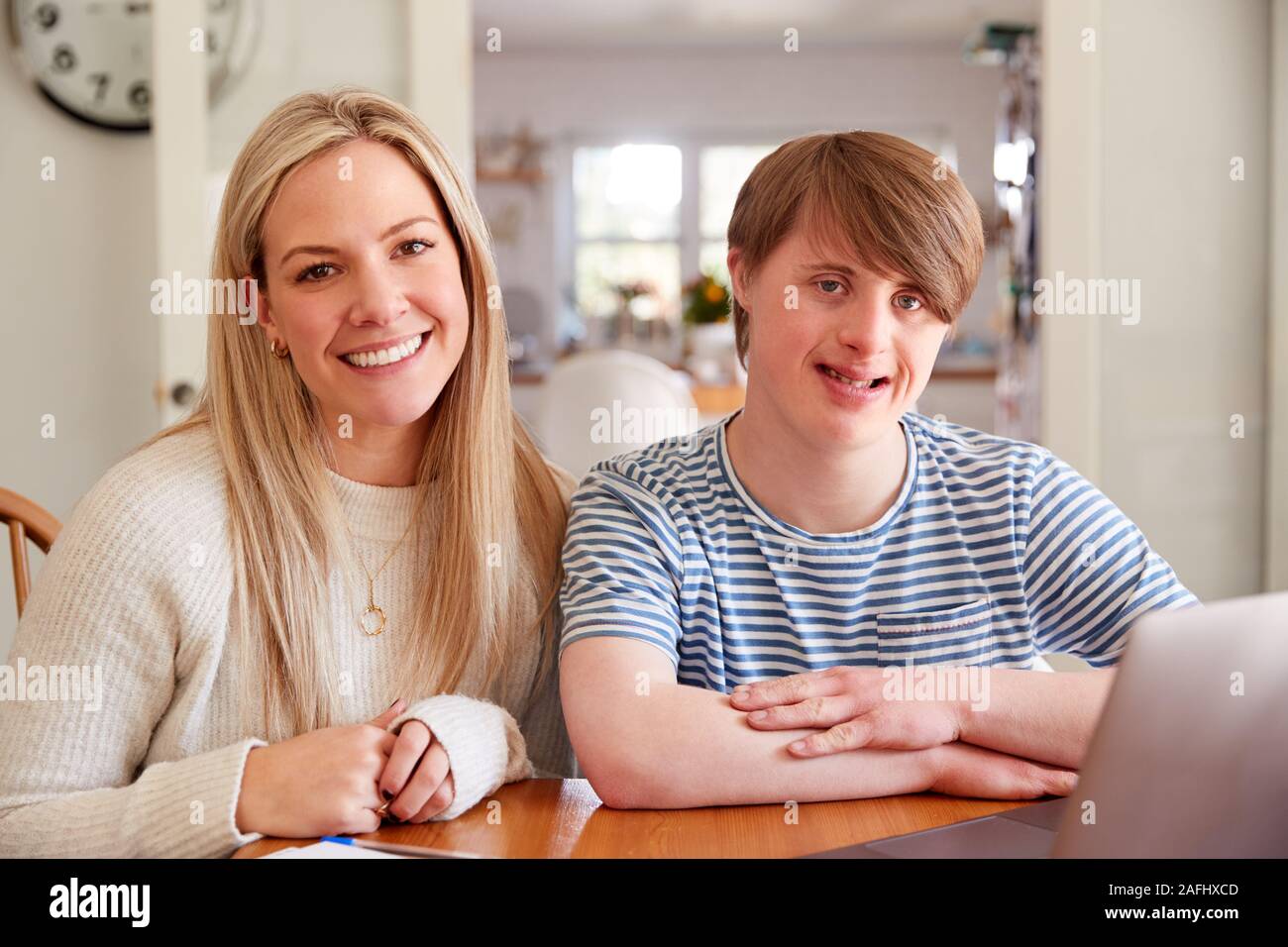 Portrait Of Downs Syndrome Man Sitting With Home Tutor Using Laptop For Lesson At Home Stock Photo