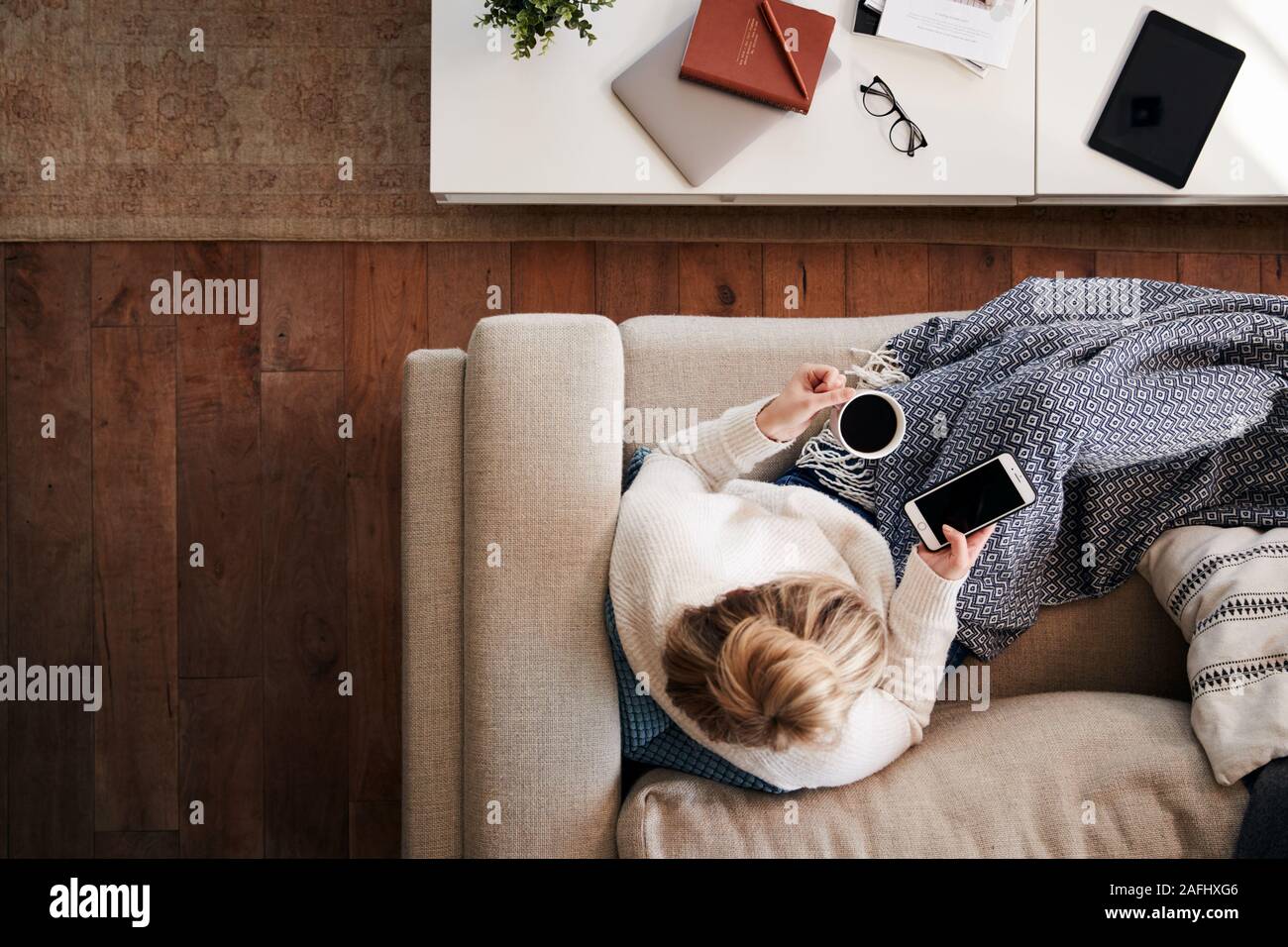 Overhead Shot Looking Down On Woman At Home Lying On Sofa Using Mobile Phone Stock Photo