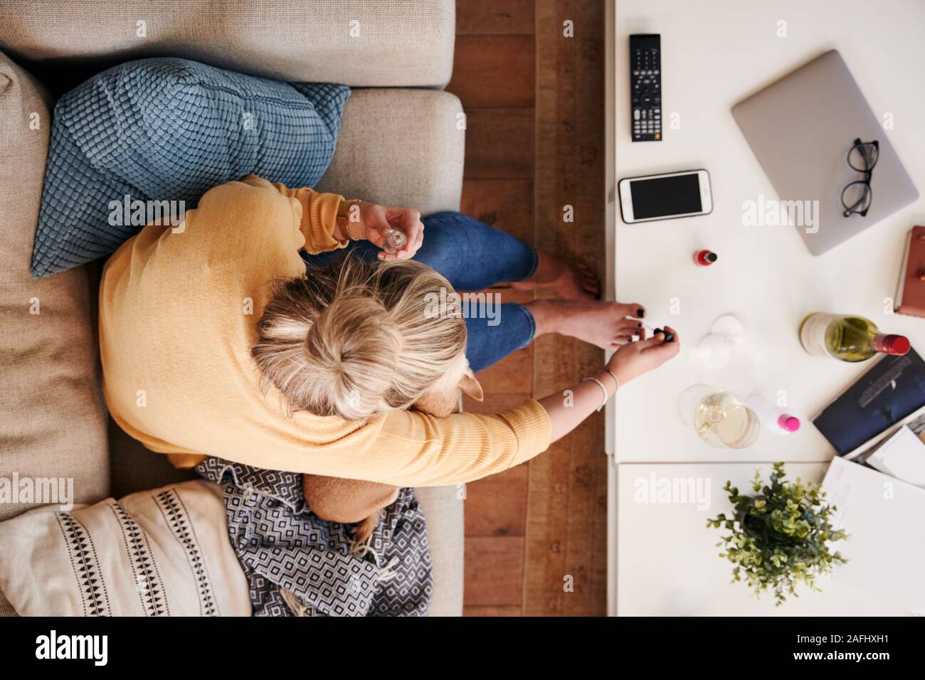 Overhead Shot Looking Down On Woman At Home Lying On Sofa Painting Toe Nails Stock Photo