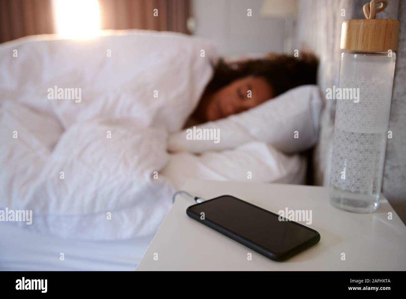 Woman Asleep In Bed With Mobile Phone On Bedside Table Stock Photo