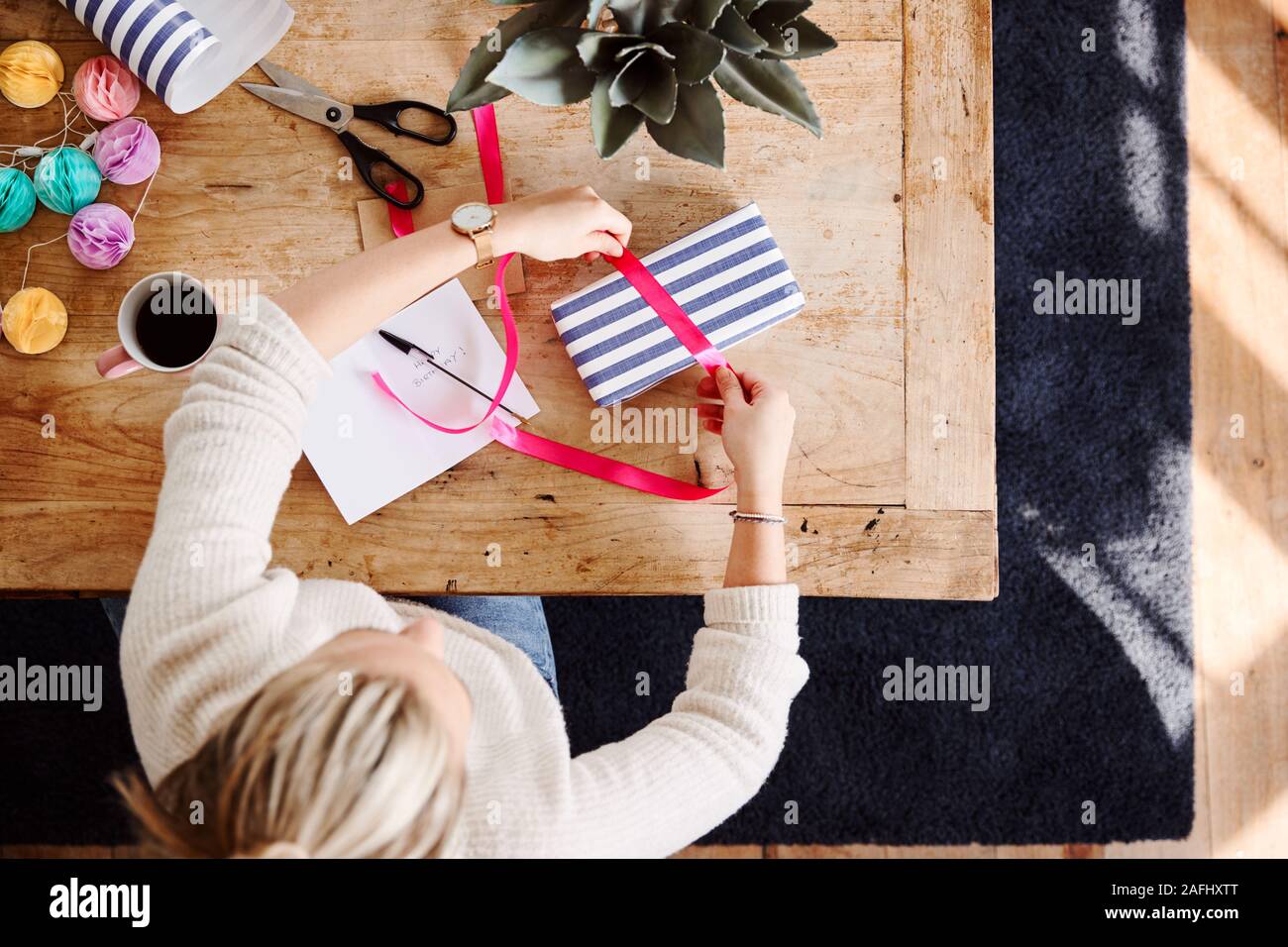 Overhead Shot Looking Down On Woman At Home Wrapping Gift And Writing Birthday Card Stock Photo