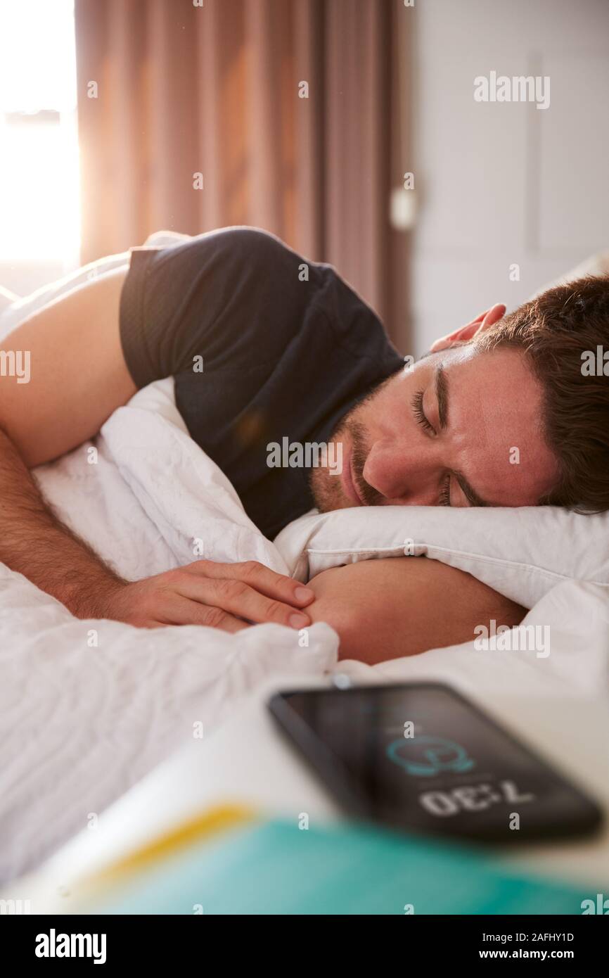 Man Asleep In Bed With Mobile Phone On Bedside Table Stock Photo