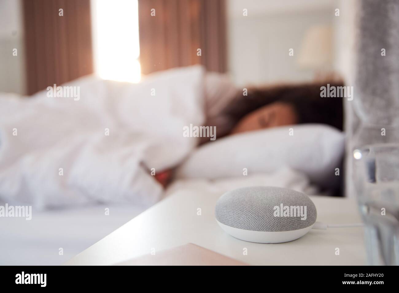Woman Sleeping In Bed With Voice Assistant On Bedside Table Next To Her Stock Photo