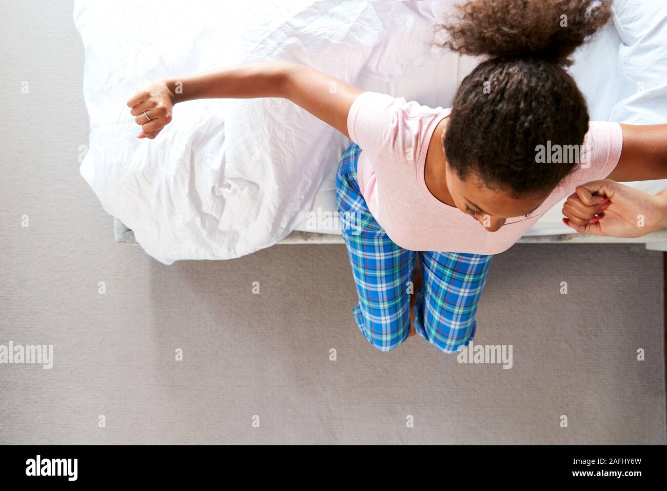 Overhead View Of Woman Wearing Pajamas Stretching As She Gets Out Of Bed At Home Stock Photo