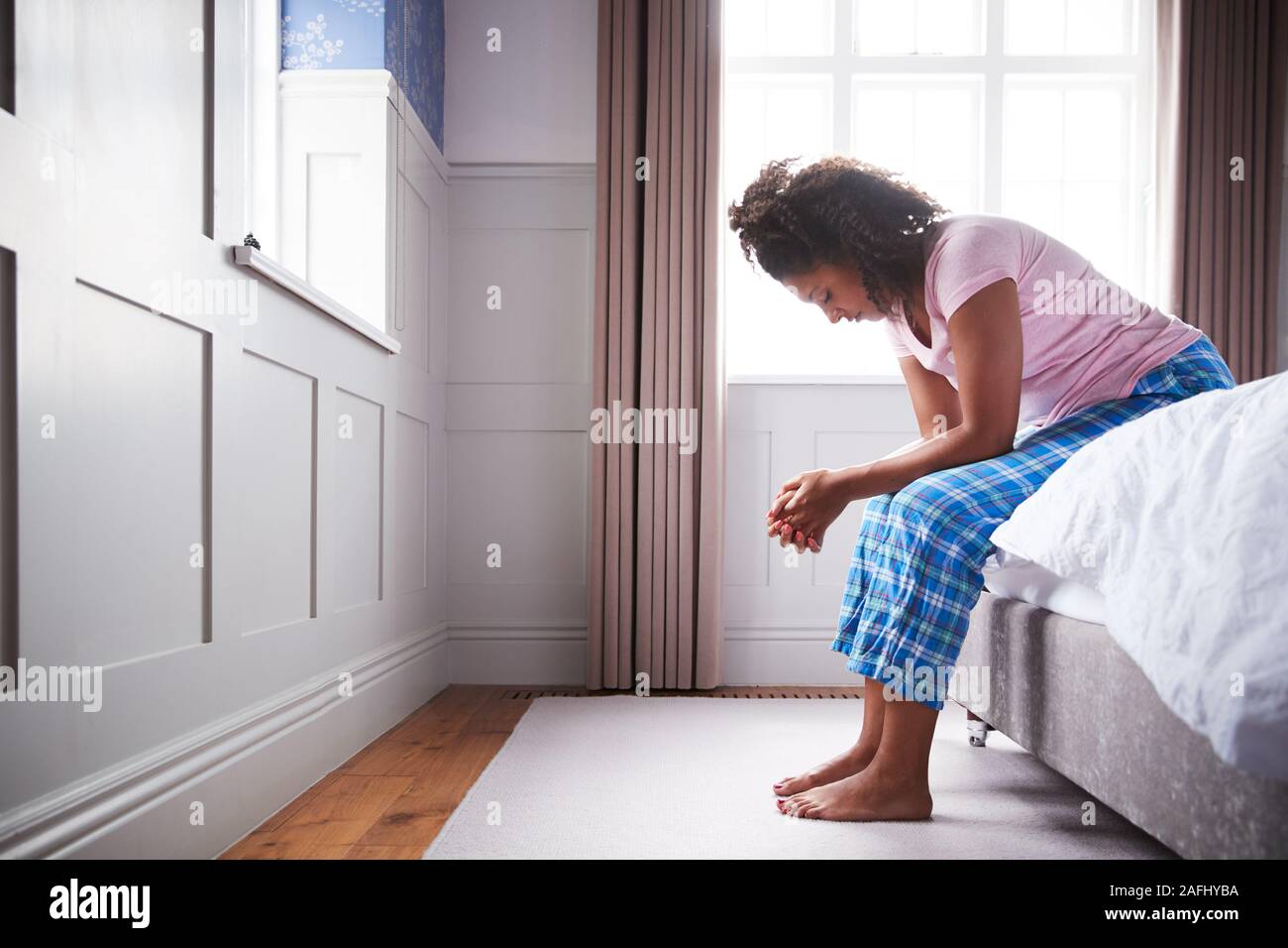 Woman Wearing Pajamas Suffering With Depression Sitting On Bed At Home Stock Photo